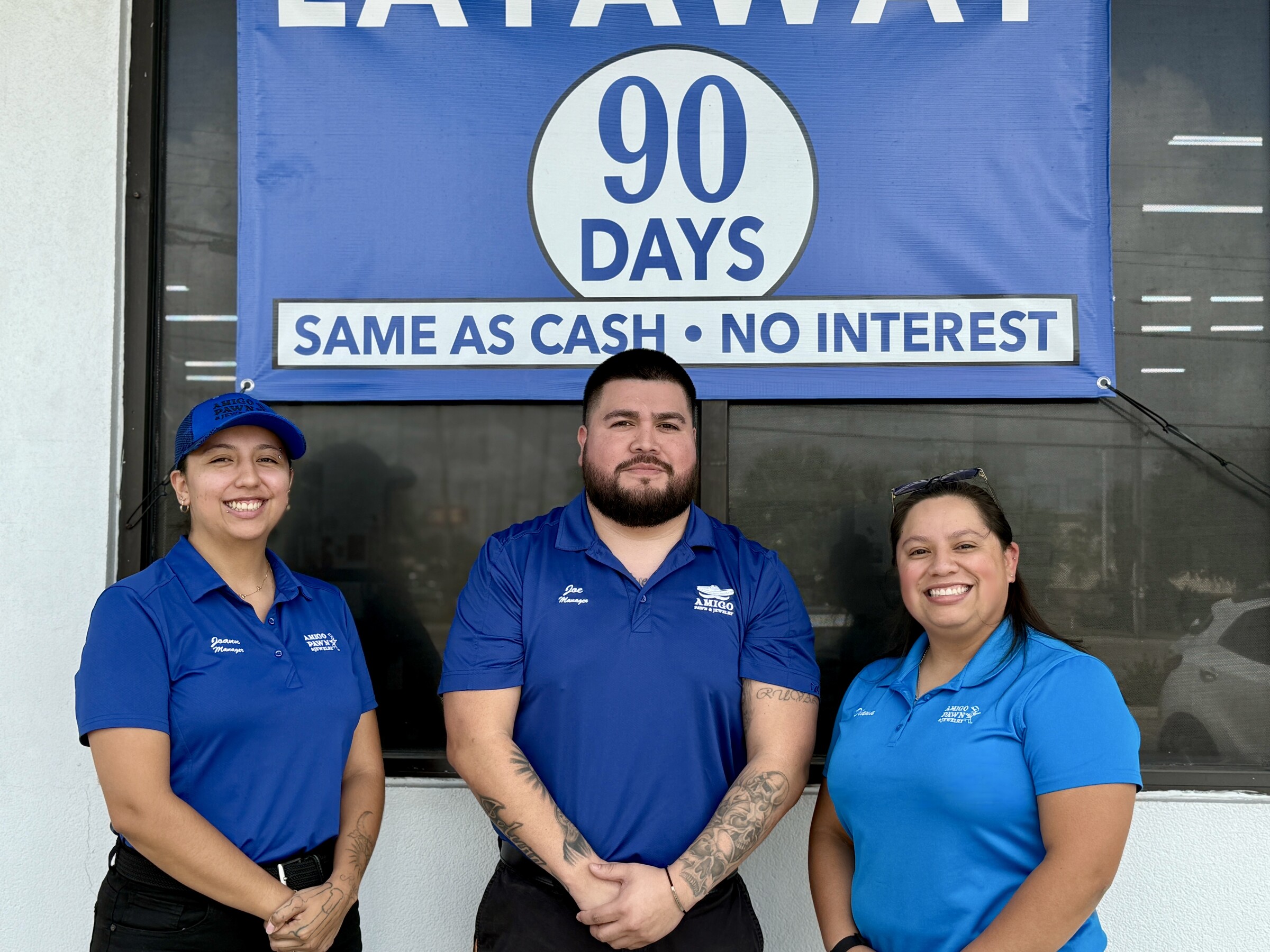 Three Amigo team members posing in front of a layaway banner